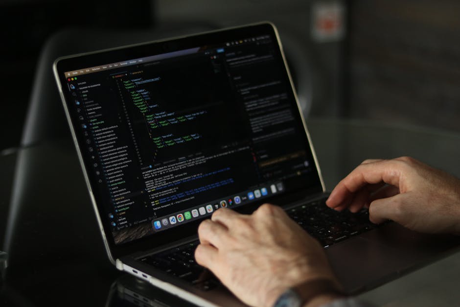 A close-up image showing a laptop on a wooden surface with visible code on the screen, indicating a programming or web development activity. Next to the laptop, there is a ceramic coffee mug with the 