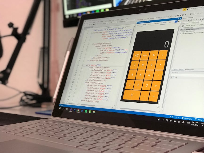 Close-up of a silver laptop displaying a coding window with HTML and CSS code on the left side of the screen, and a large orange calculator interface with black buttons and digital display on the righ